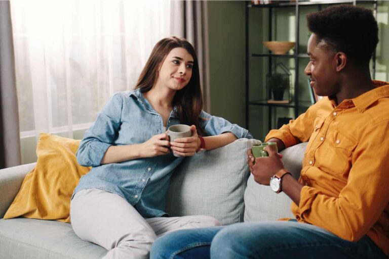 a man and a woman sit on the couch drinking coffee and talking