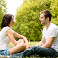 a smiling man and woman sitting on the grass holding hands and talking