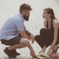 man looking girl in eyes while helping her to pick up dropped books on the street