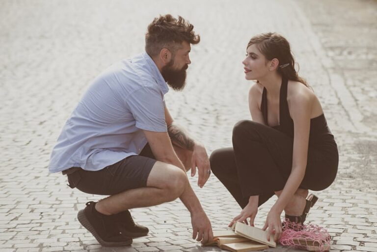 man looking girl in eyes while helping her to pick up dropped books on the street