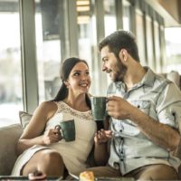 a smiling man and woman sit in a cafe and drink coffee