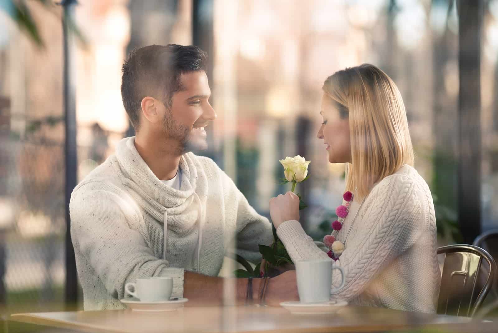 a man and a woman sit at a table and talk over coffee