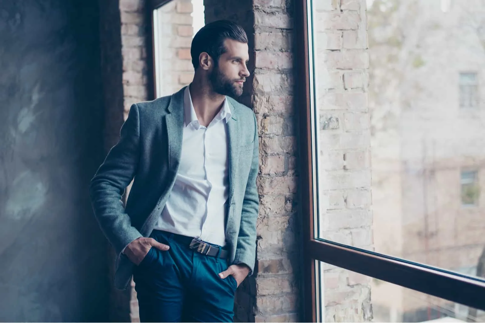 Stylish young bearded man is standing near the window