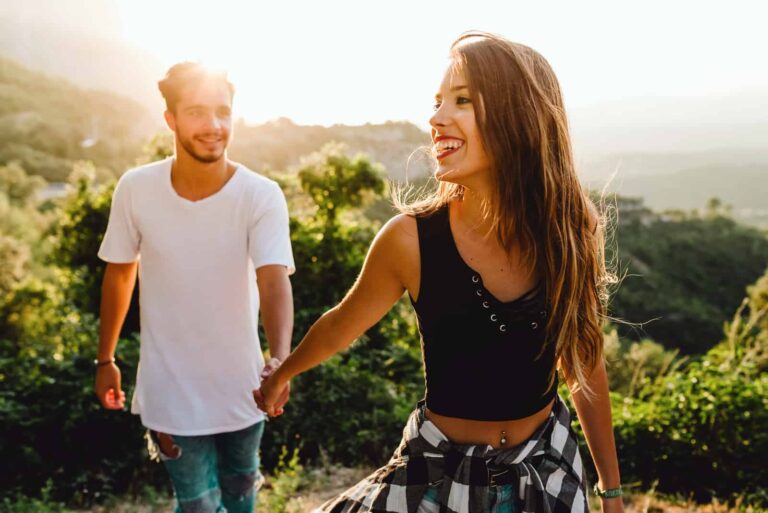 a smiling couple in love holding hands and walking through the park