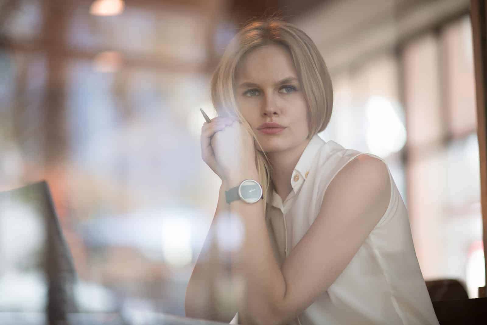 a blonde-haired woman sits pensively at work