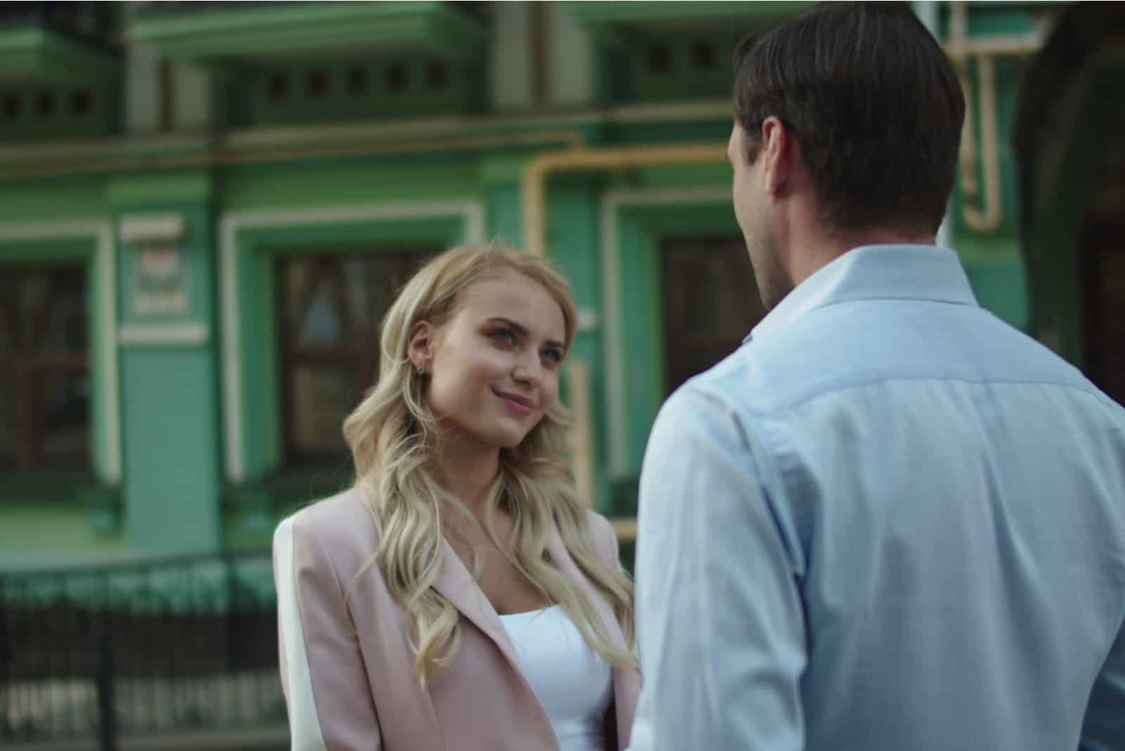 a blonde-haired woman stands on the street talking to a man