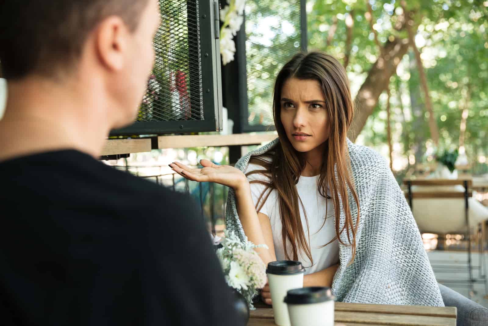 a confused woman sits at a table and talks to a man