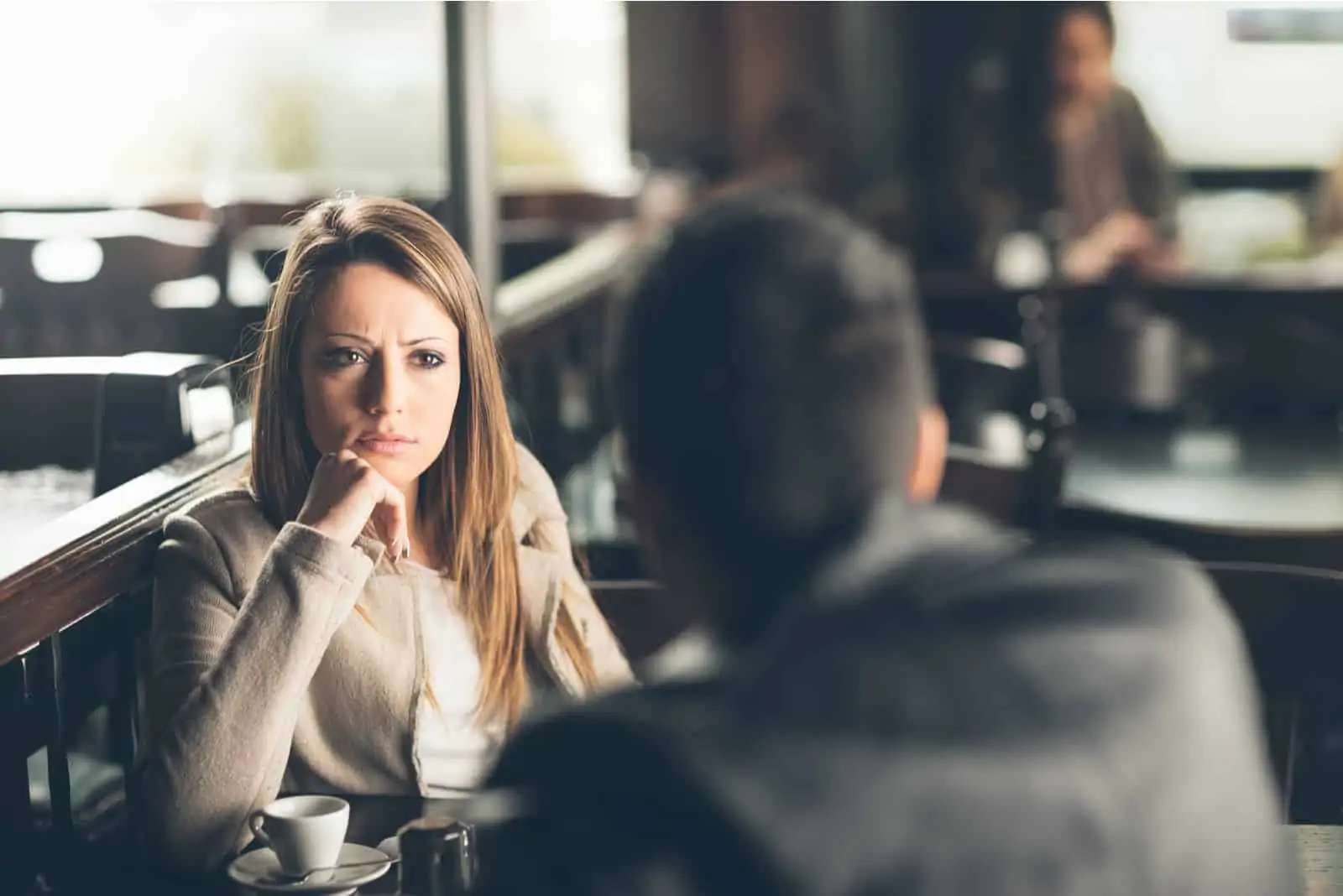a confused woman sits at a table and talks to a man