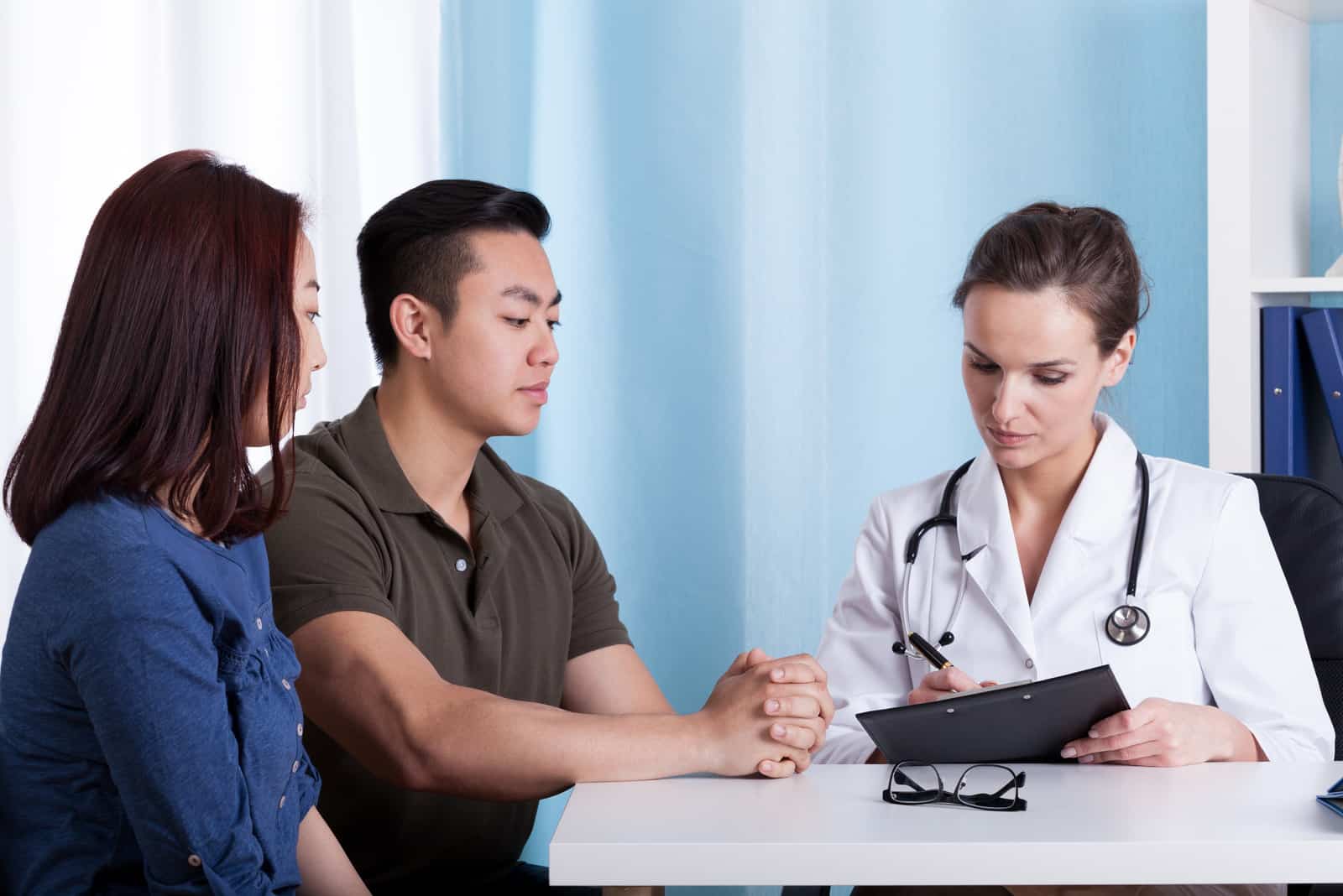 um homem e uma mulher estão sentados à mesa com um médico enquanto conversam