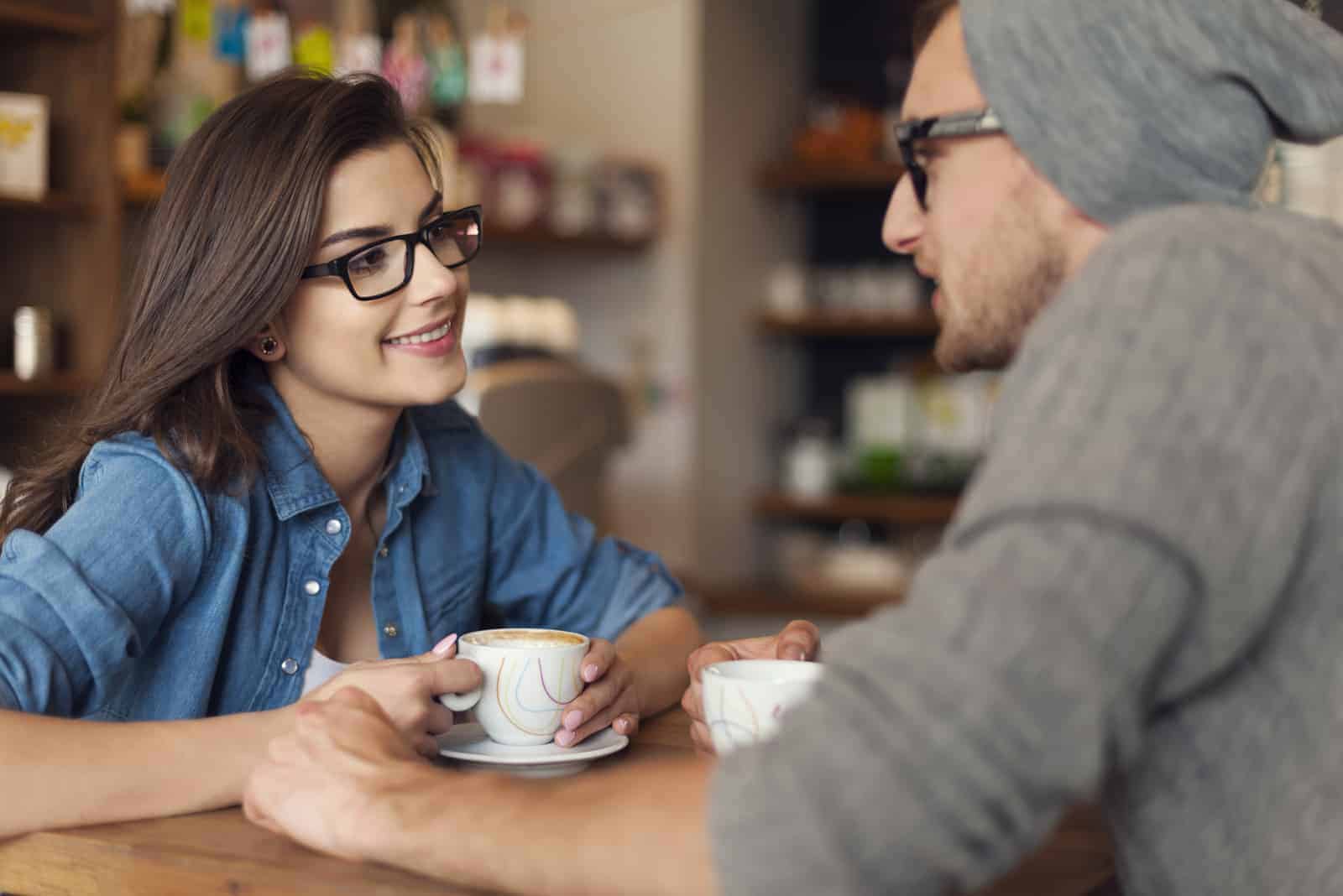 un hombre y una mujer están sentados en una cafetería tomando café hablando