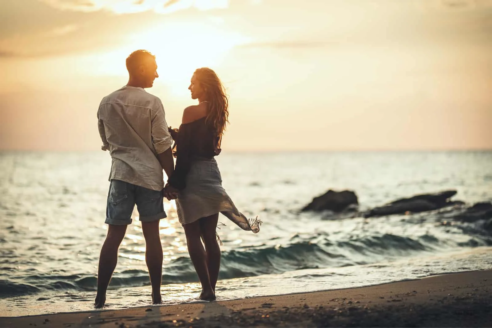 a man and a woman are standing on the beach by the sea holding hands
