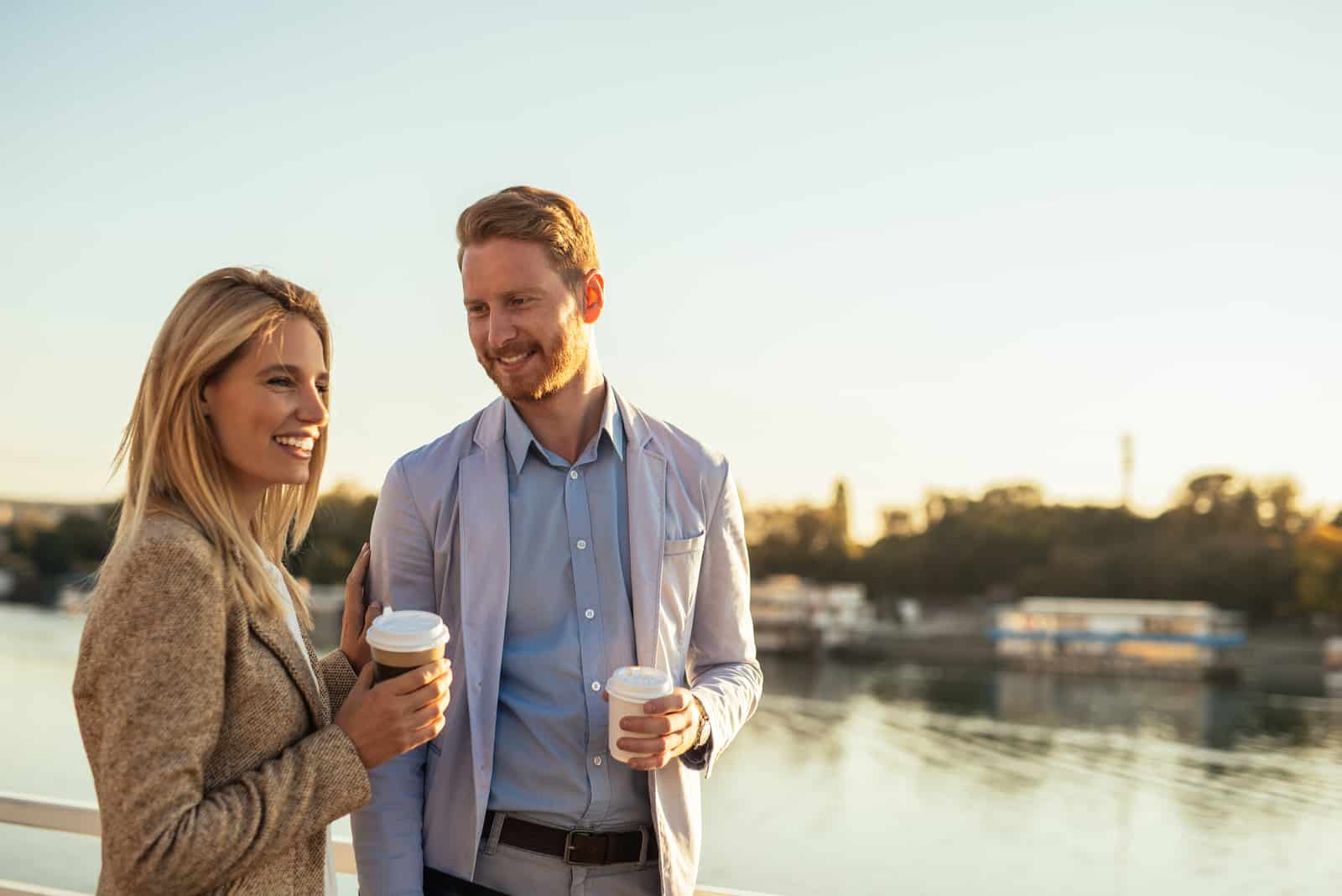a man and a woman hold coffee in their hands and talk