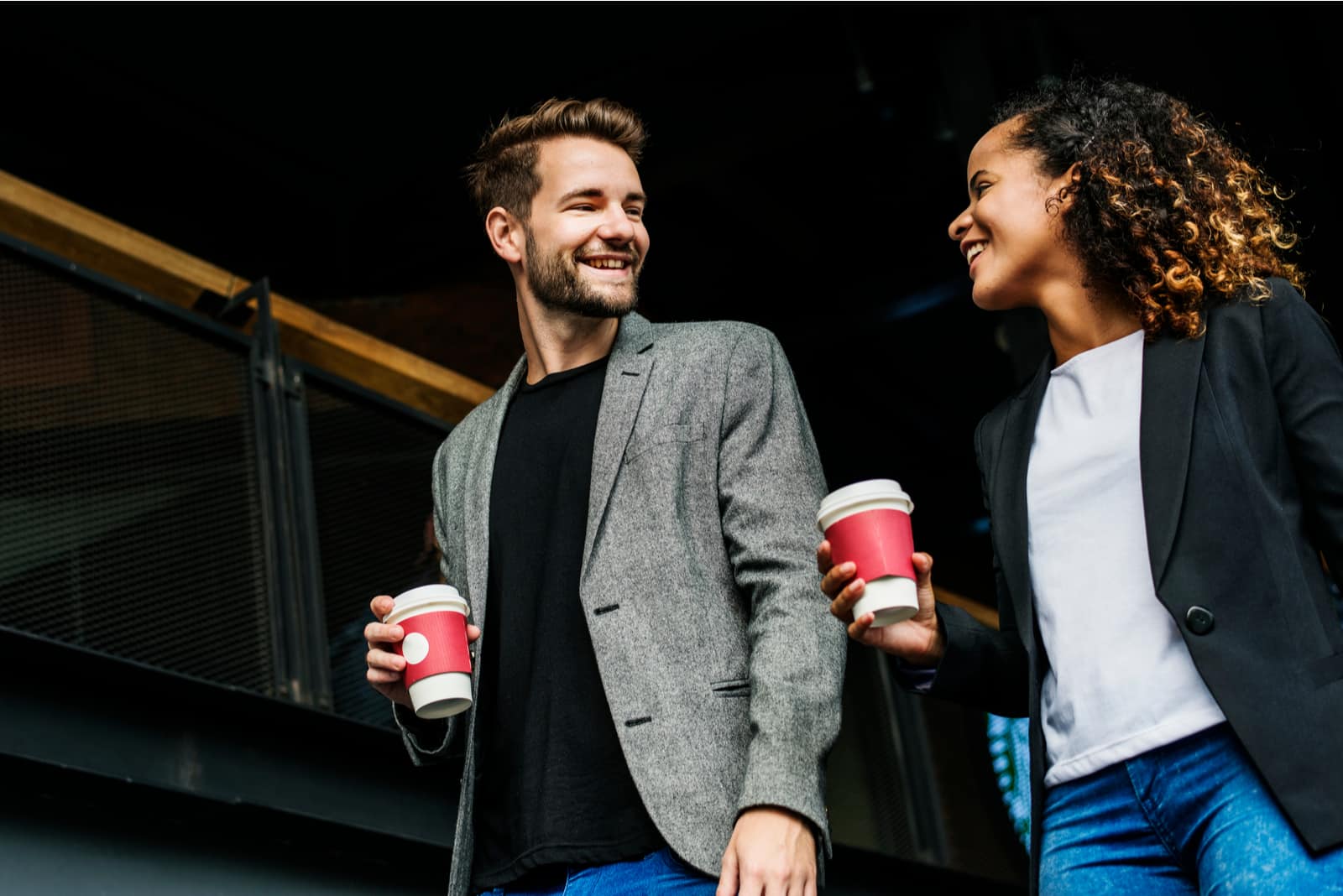 a man and a woman holding coffee in their hands and walking