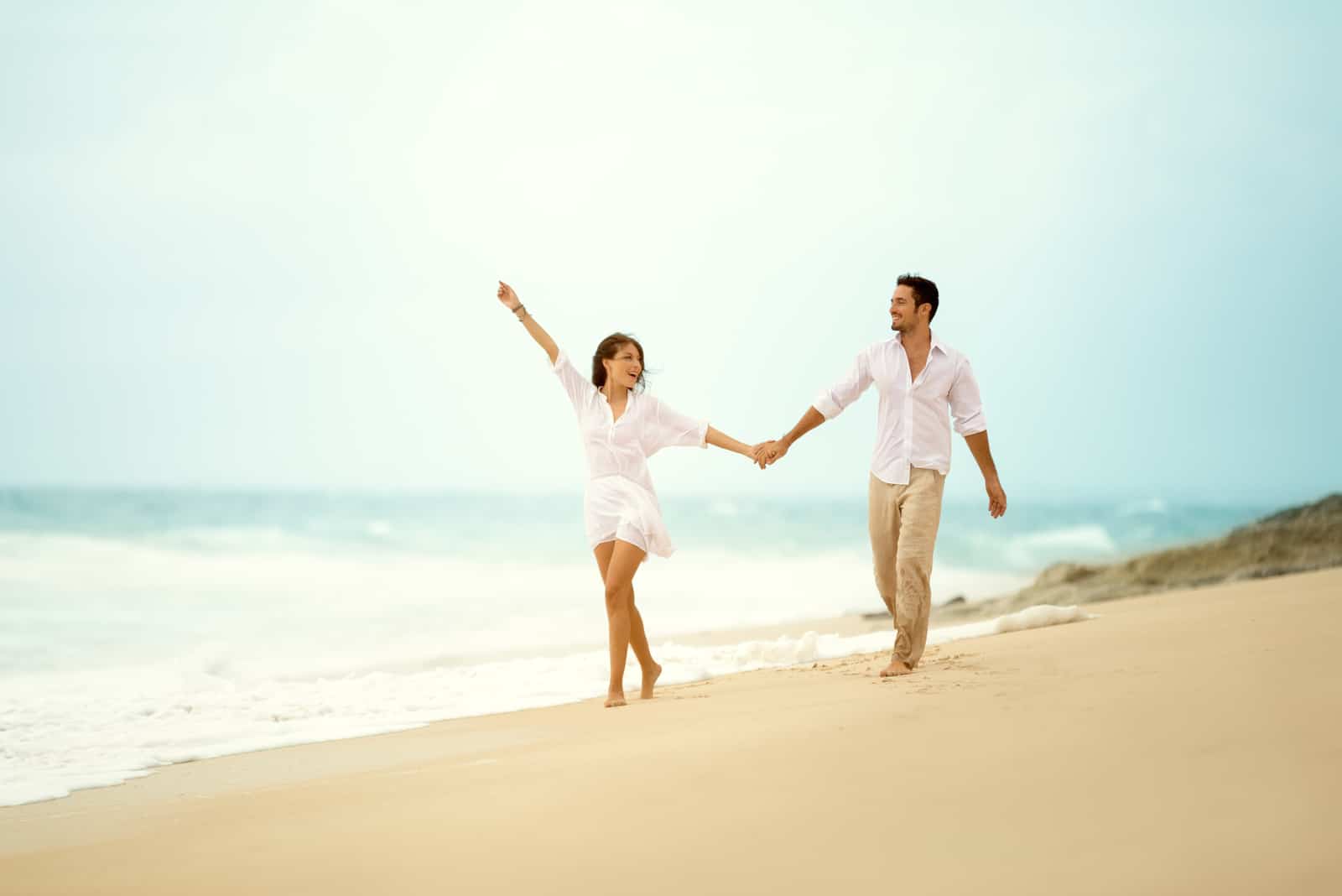 a man and a woman holding hands and walking along the beach