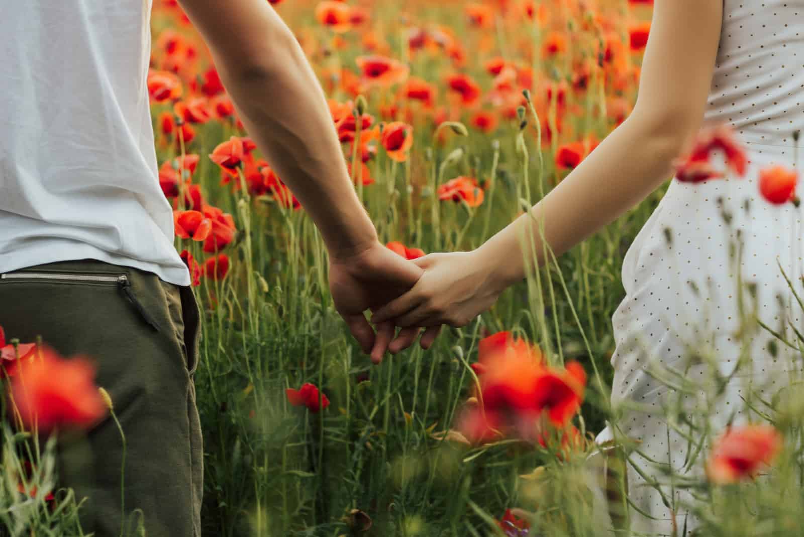 a man and a woman holding hands as they walk through the field