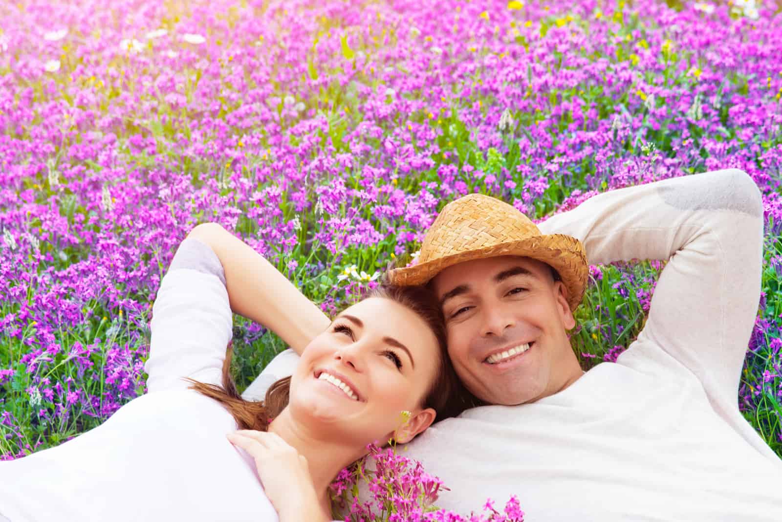 a man and a woman lie in a field of purple flowers