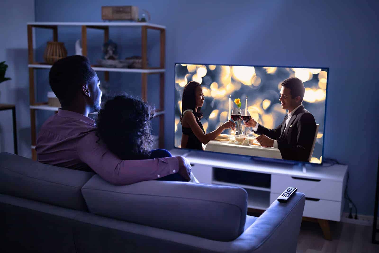 a man and a woman sit on the couch embracing and watching a movie