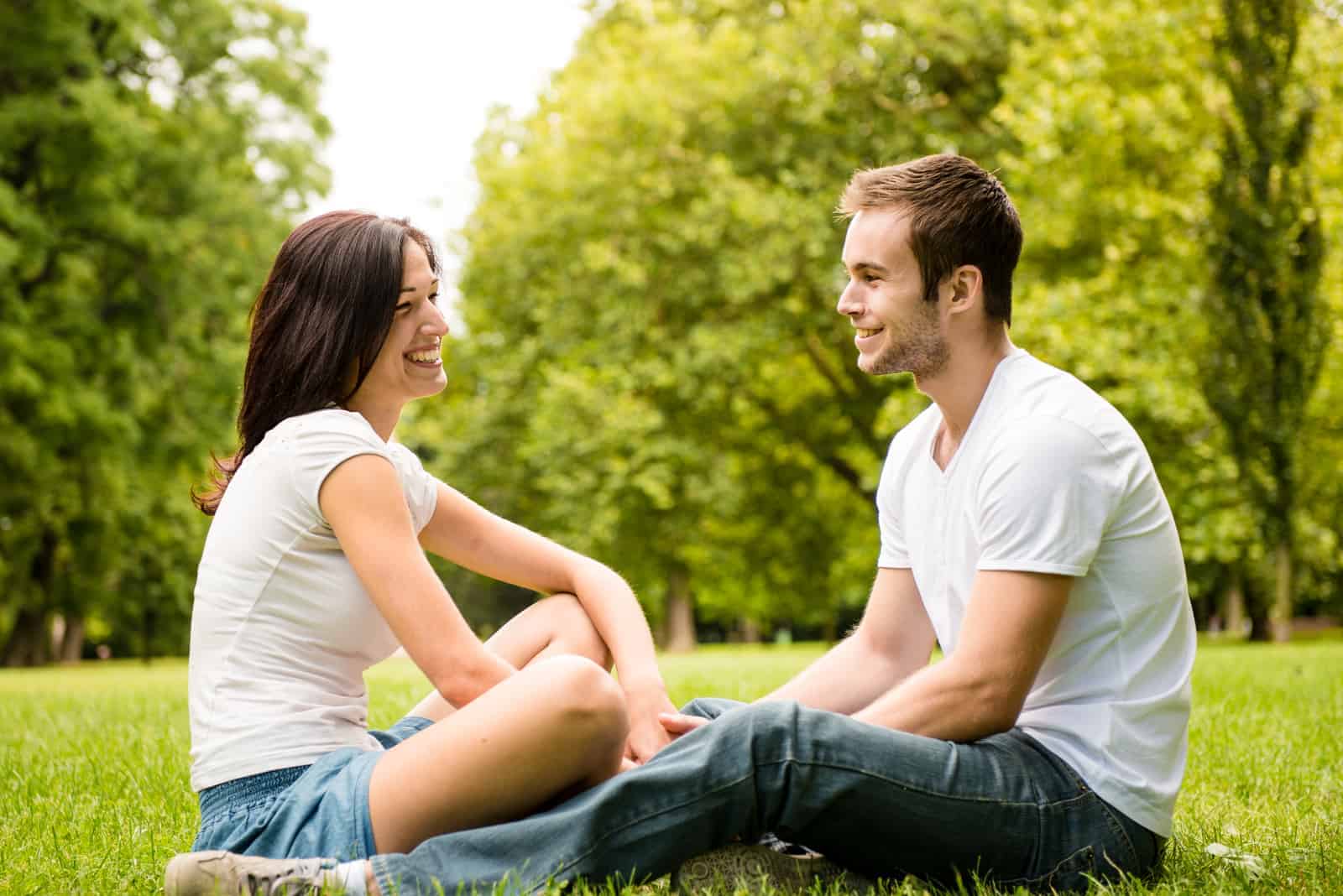 a man and a woman sit on the grass and talk