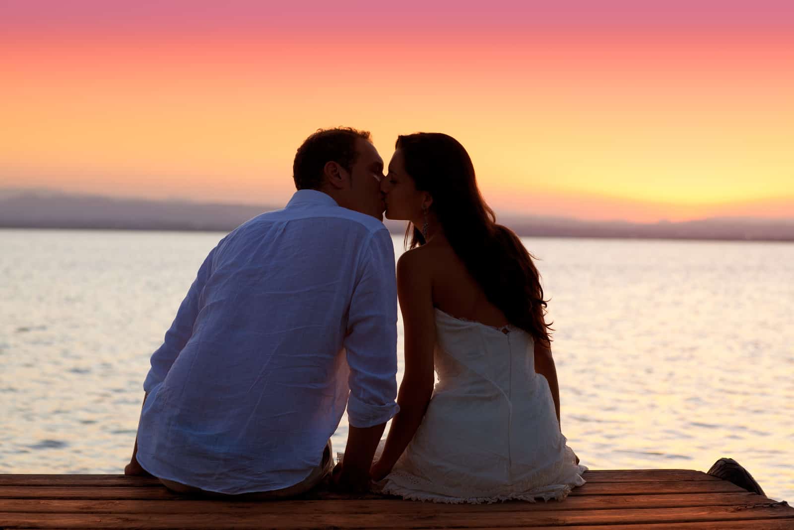 a man and a woman sit on the pier and kiss