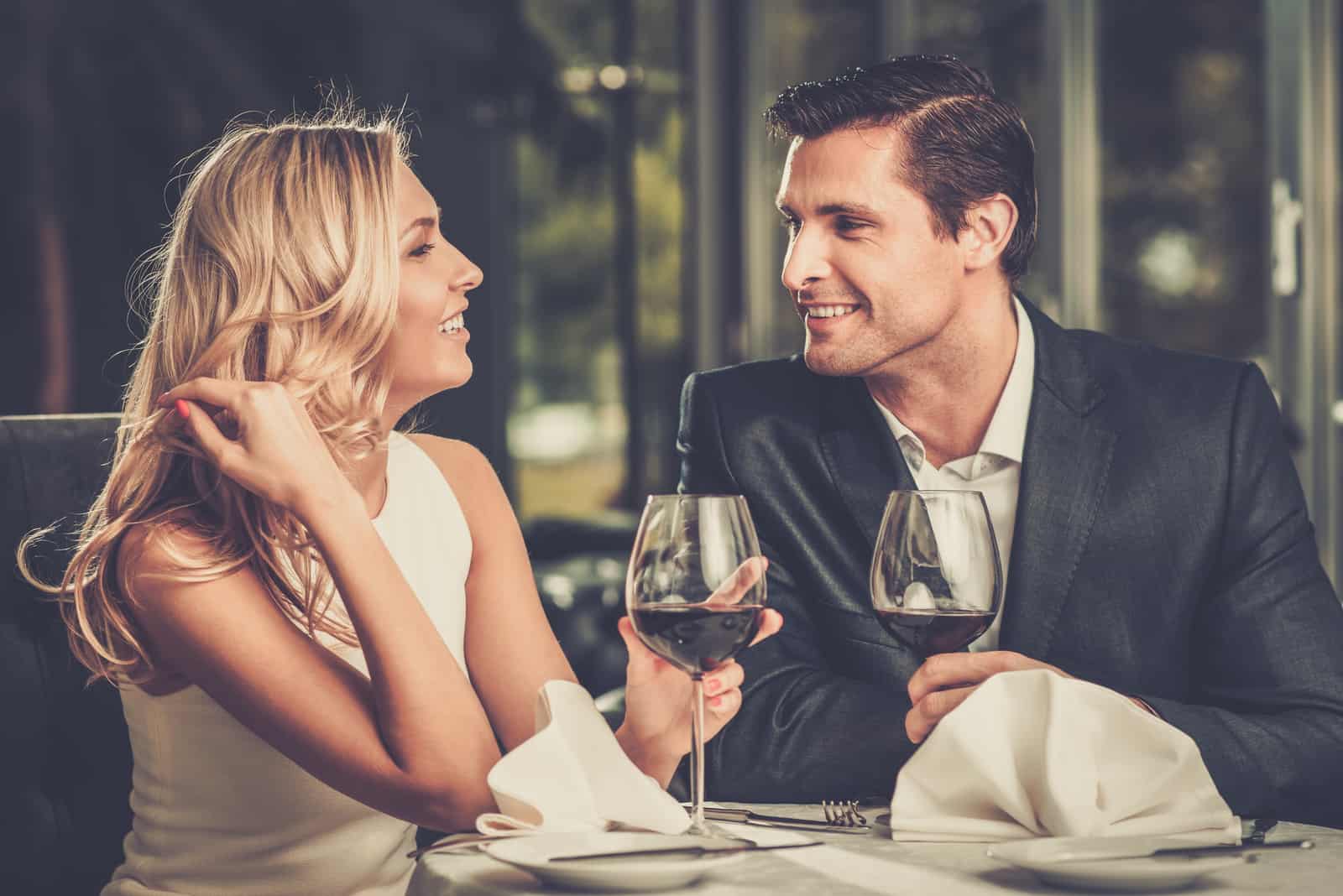 a man and a woman sitting at a table with wine talking