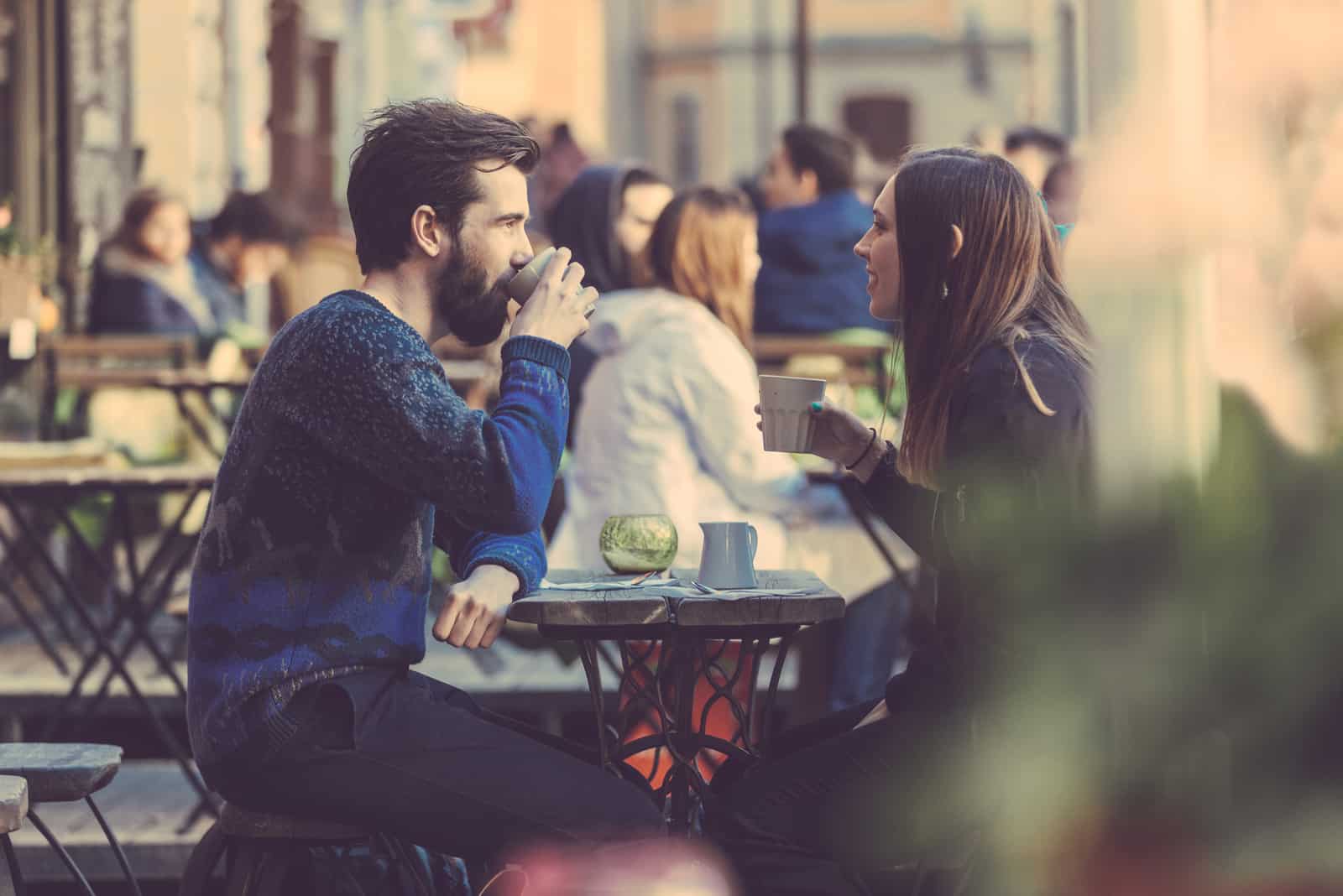 a man and a woman sitting outdoors having coffee talking