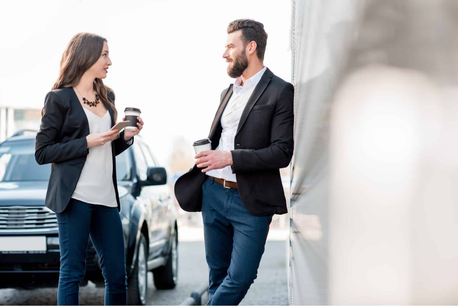 a man and a woman standing on the street holding coffee in their hands and talking