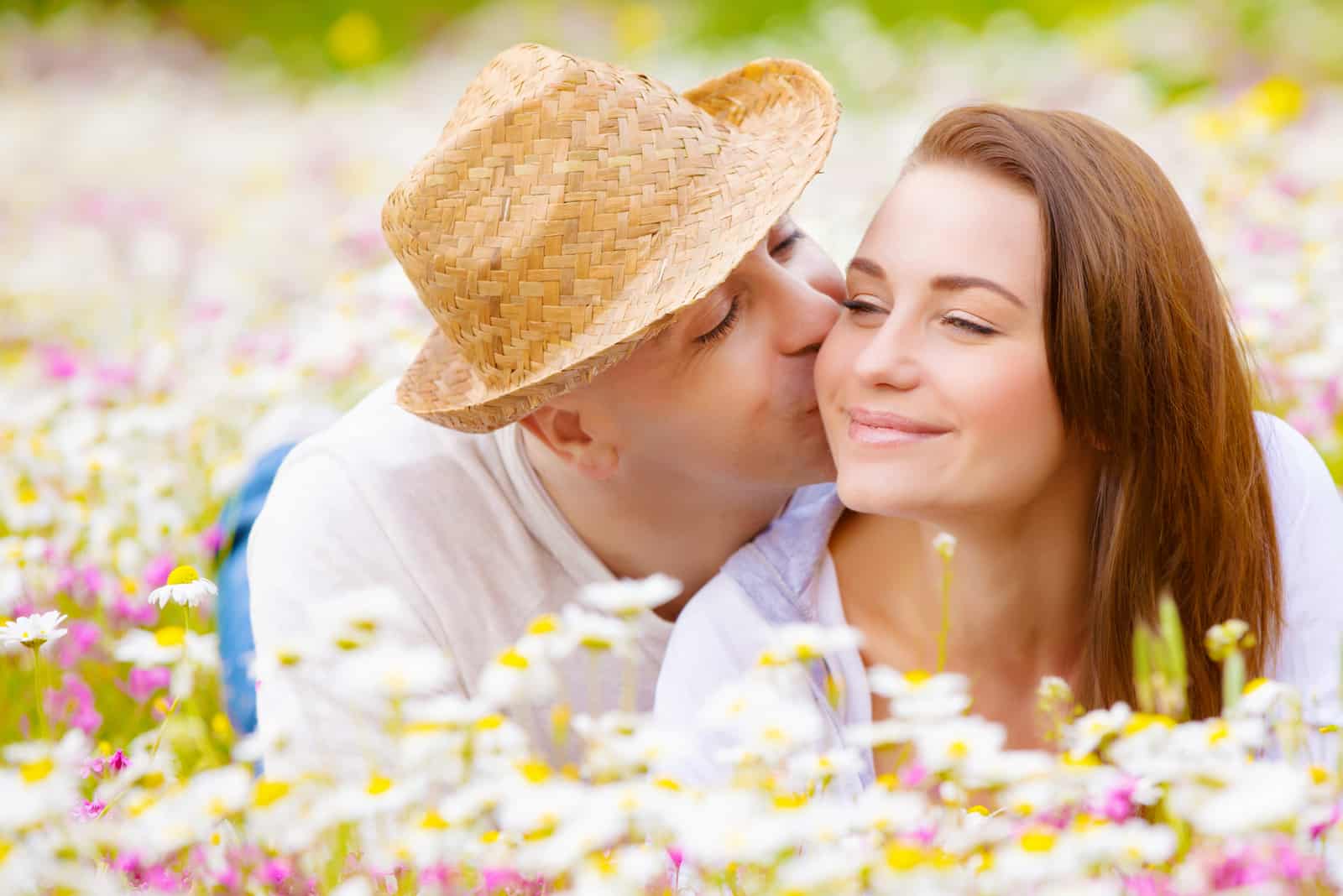 a man kisses a woman on the cheek as they lie in flowers