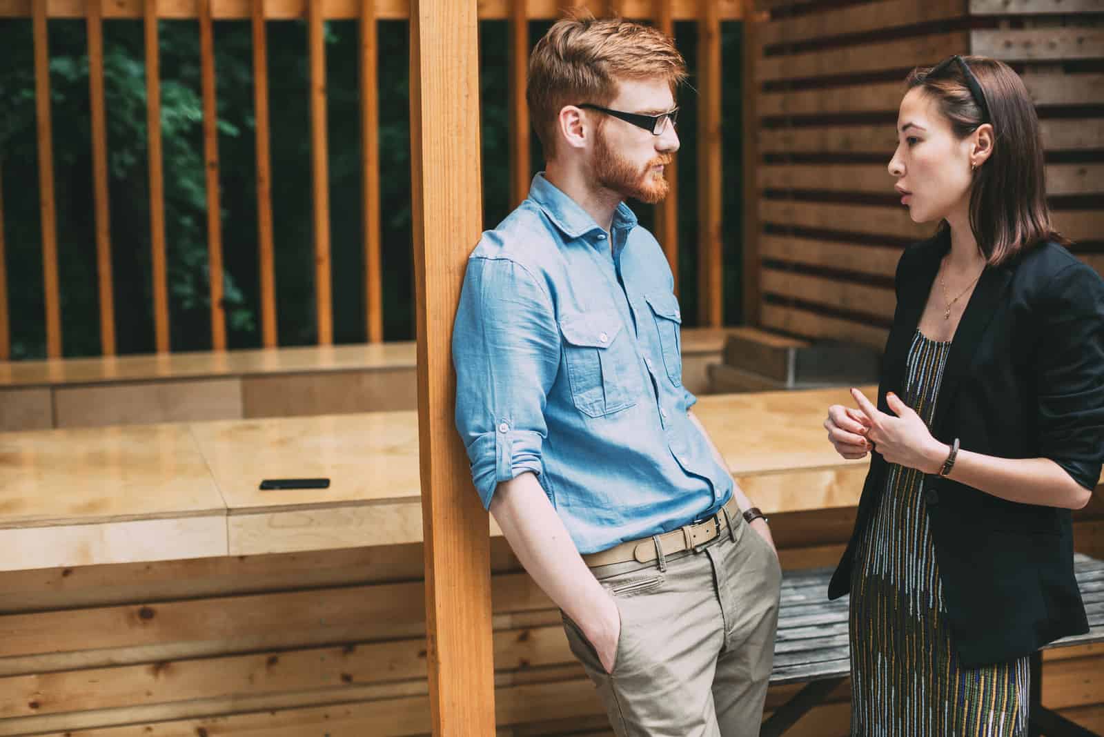 a man leaning against a fence talks to a woman