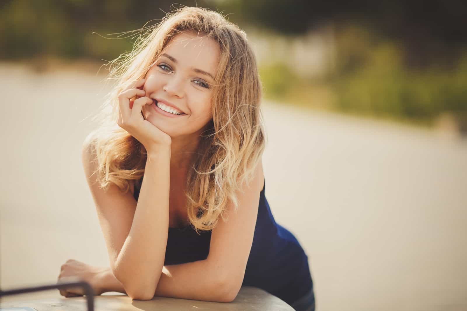 uma mulher sorridente de cabelo louro encostada a uma base de madeira