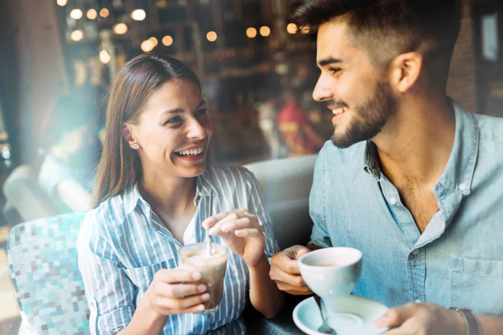 a smiling man and woman sit and talk over coffee