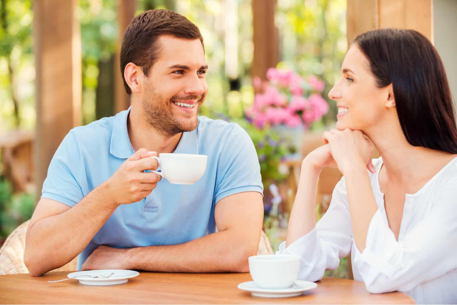 a smiling man and woman sit at a table and drink coffee