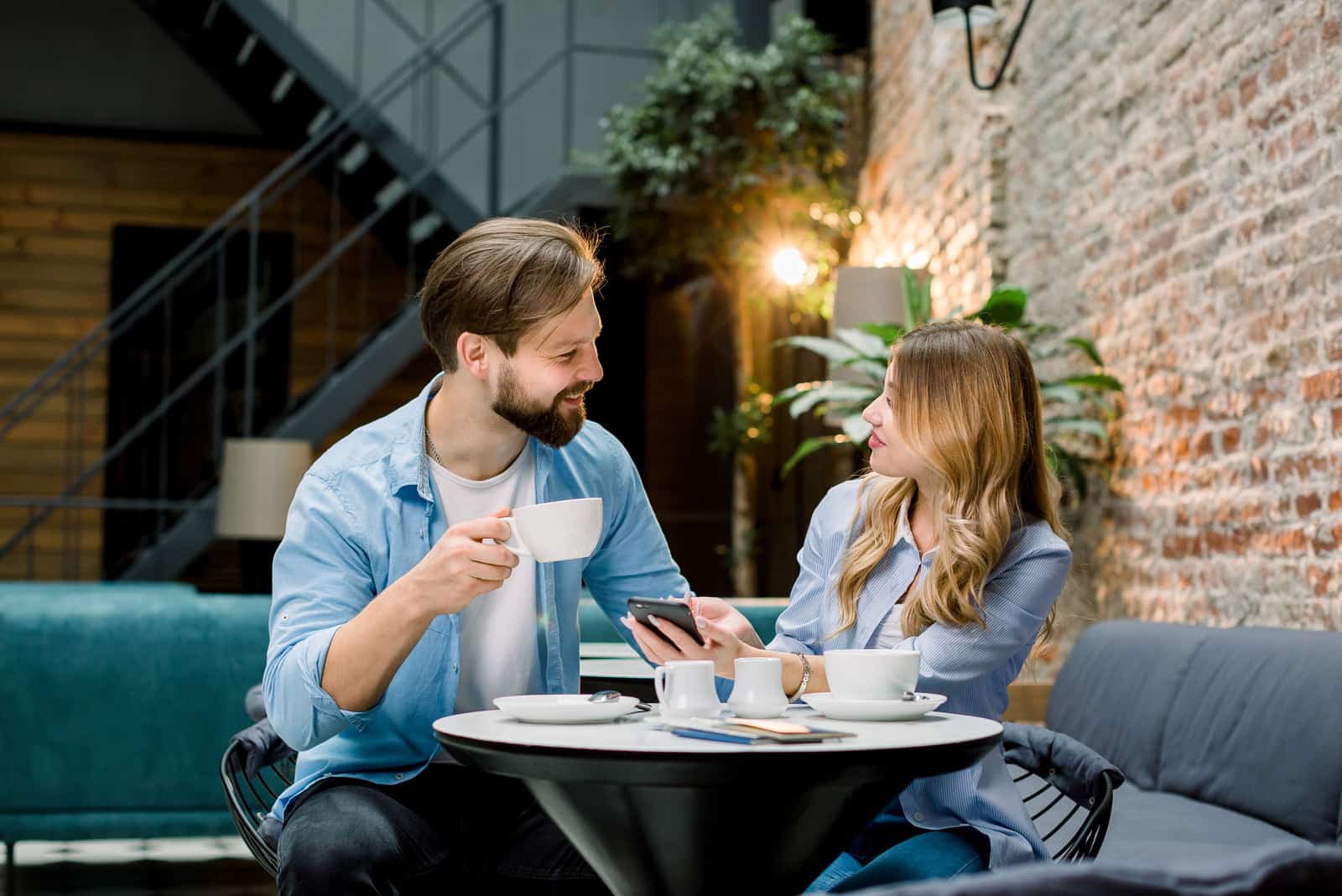 un hombre y una mujer sonrientes sentados a una mesa tomando café hablando