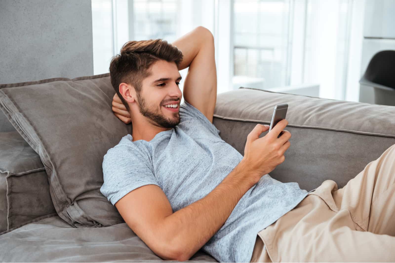 a smiling man lies on the bed and keys on the phone