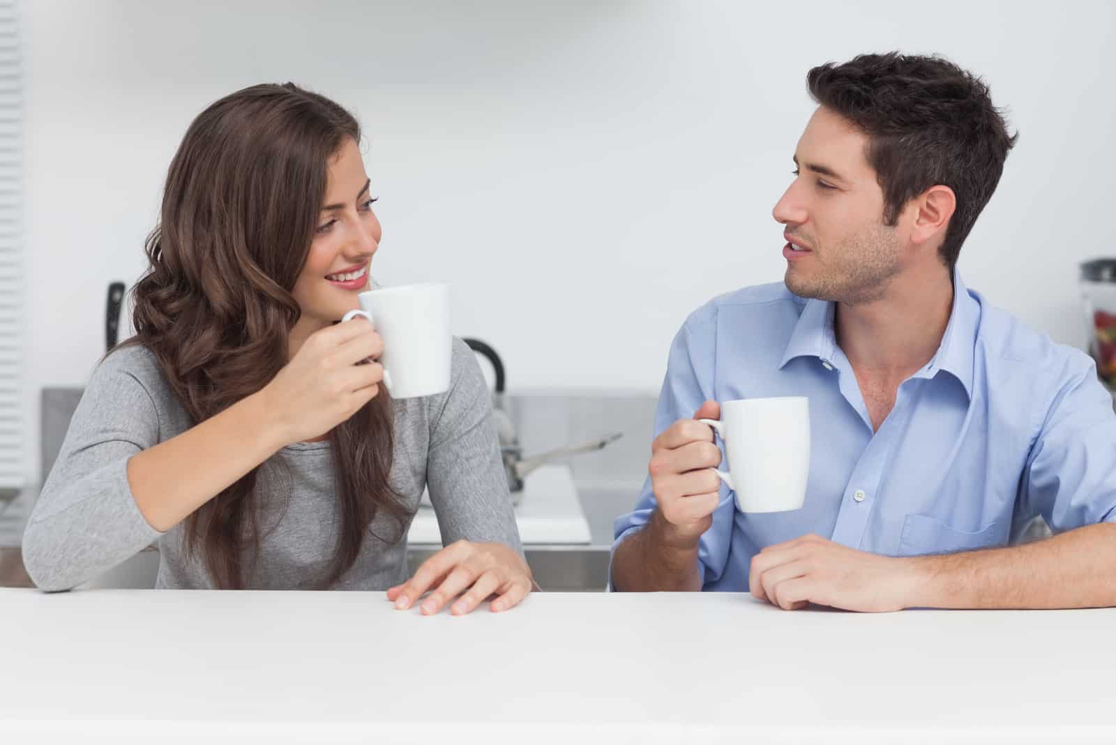 a smiling woman and a man talking while drinking coffee