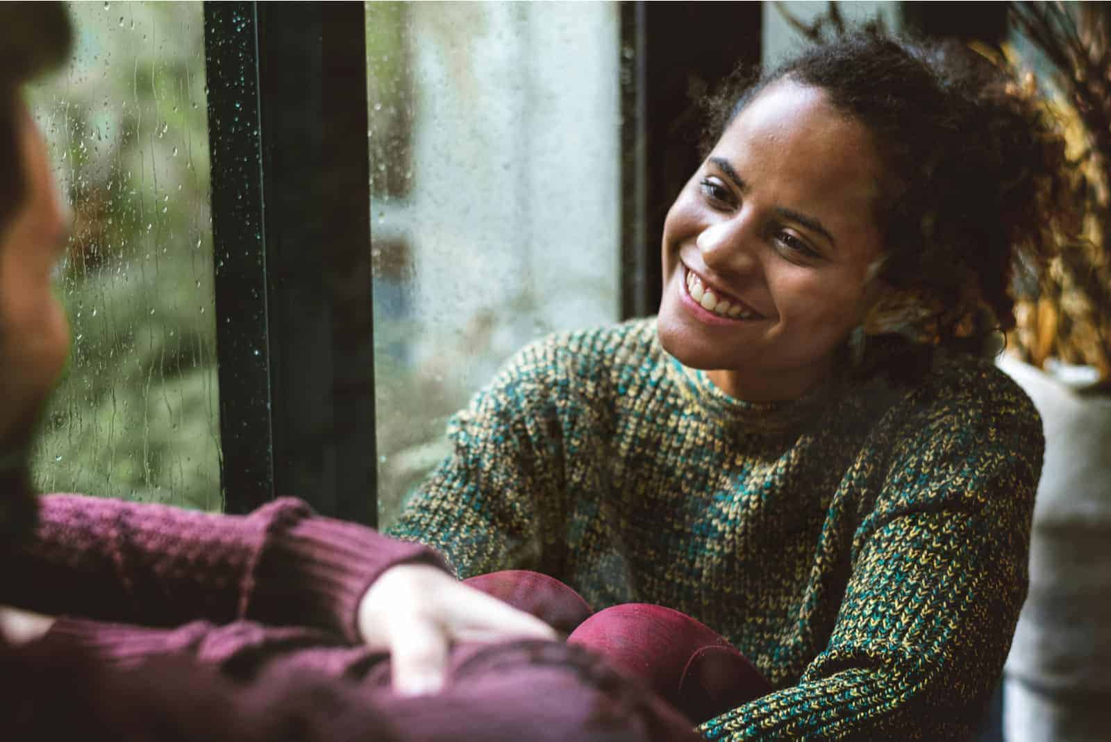 una mujer sonriente se sienta junto a la ventana y habla con la mujer