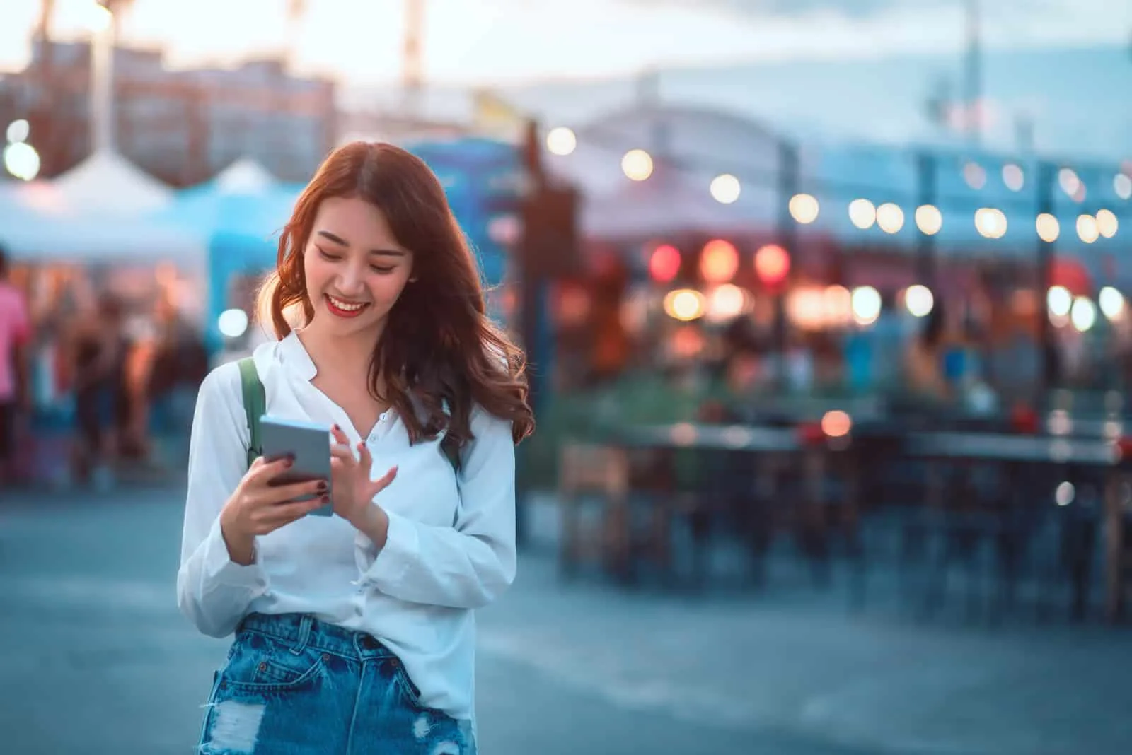 a smiling woman standing on the street and pressing a phone