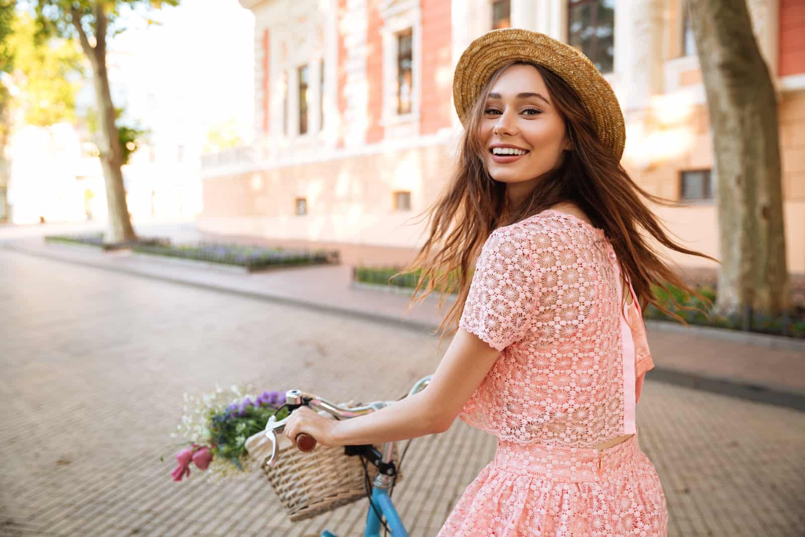 a smiling woman with a hat on her head rides a bicycle
