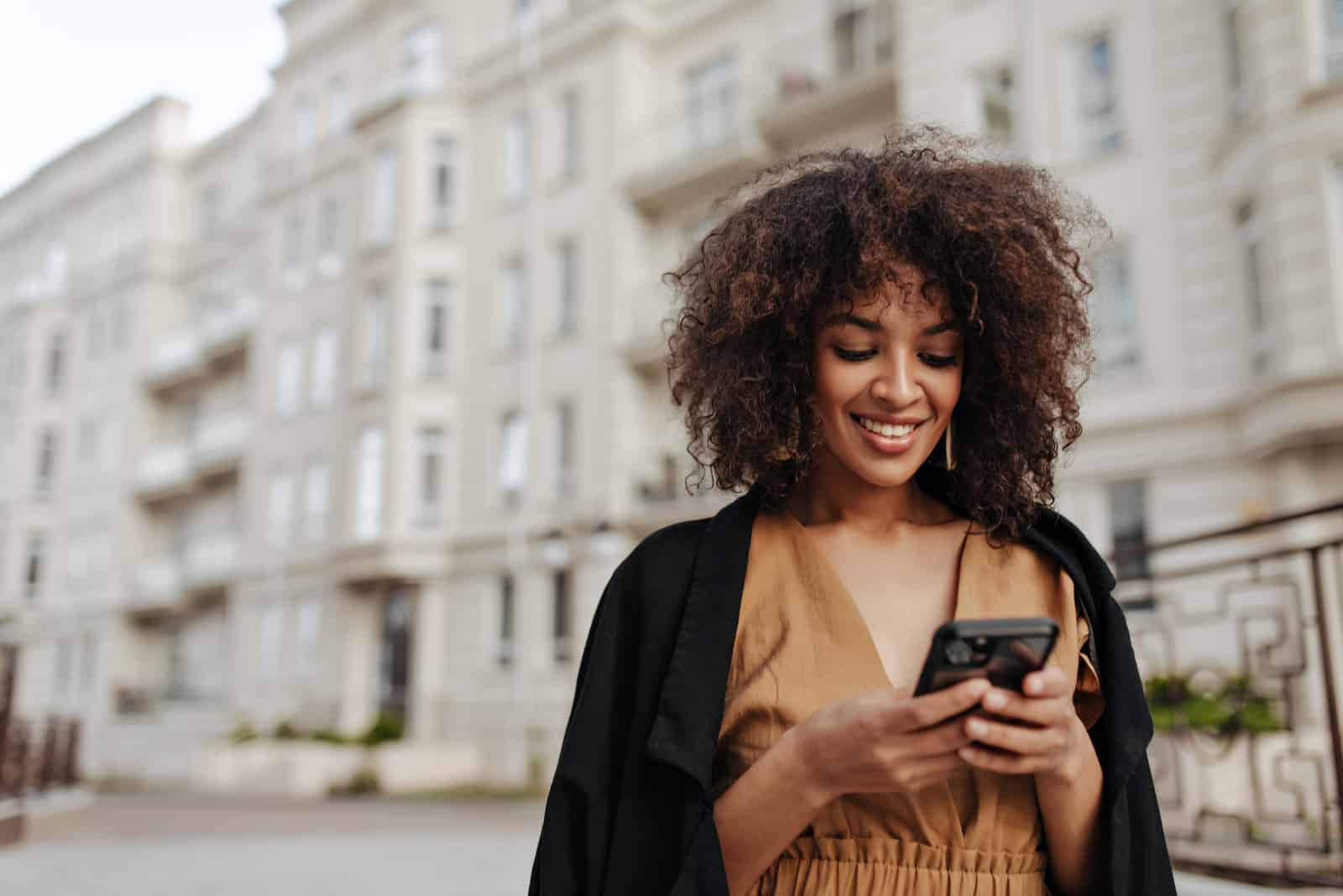 a smiling woman with frizzy hair stands on the street and buttons on the phone