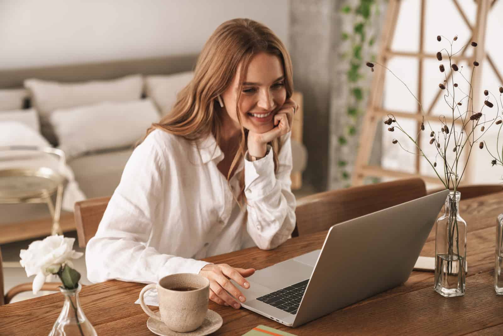 una donna sorridente con lunghi capelli castani è seduta dietro un computer portatile