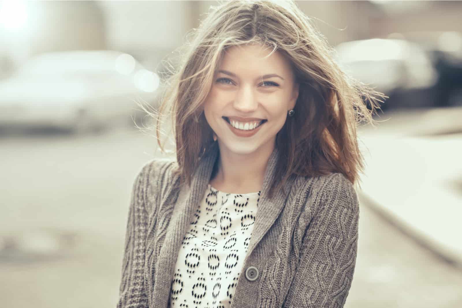 una mujer sonriente con el pelo largo y castaño se para en la calle