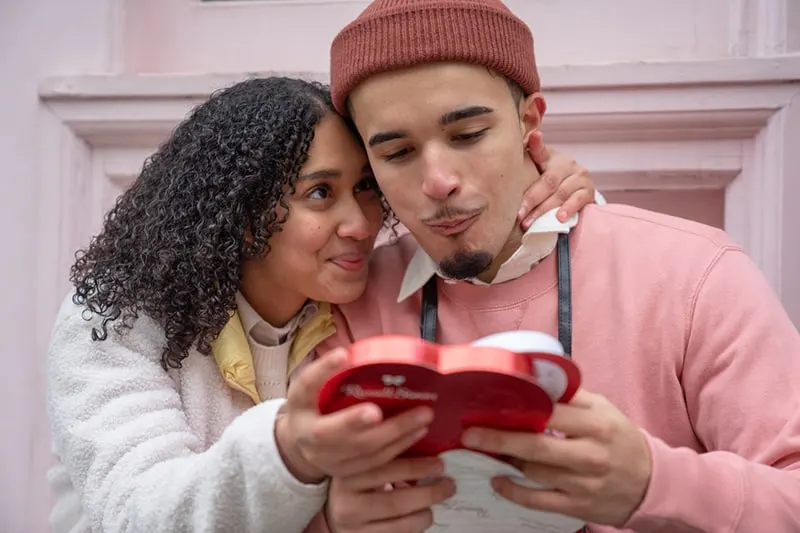 a woman gives chocolate to her boyfriend on the street celebrating their anniversary