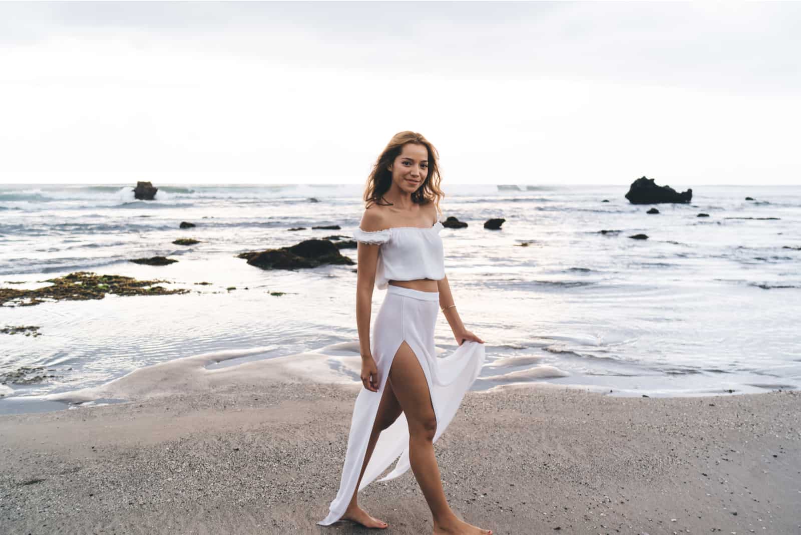 una donna in abito bianco cammina sulla spiaggia