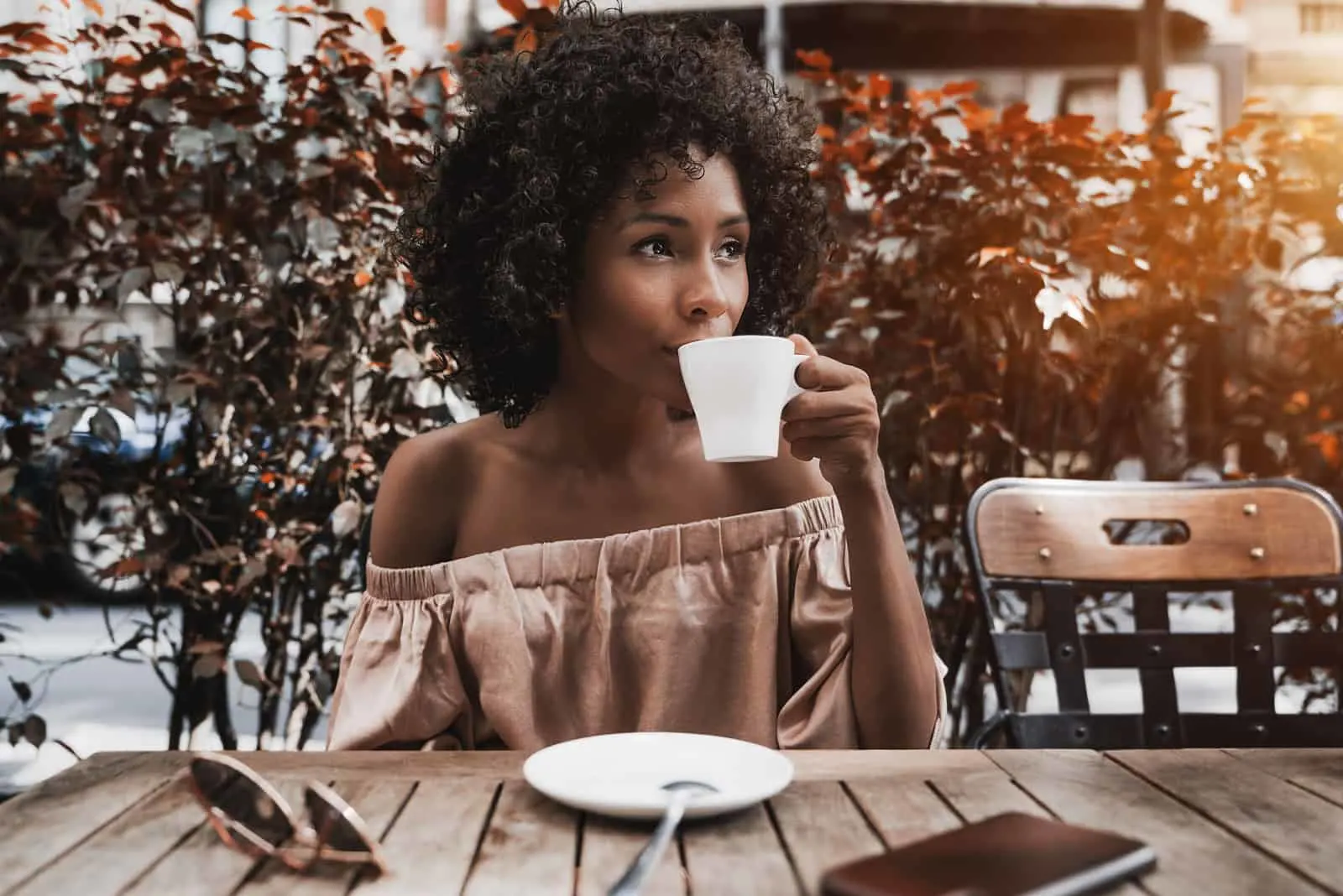 a woman with frizzy hair sits at a table drinking coffee and looks away