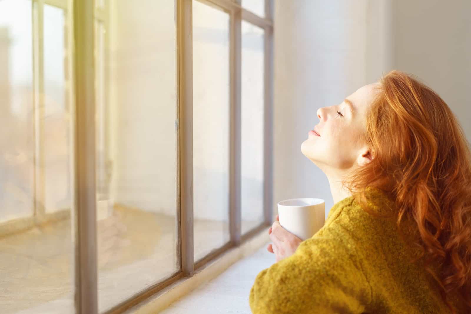 a woman with her head held high sits by the window and drinks coffee