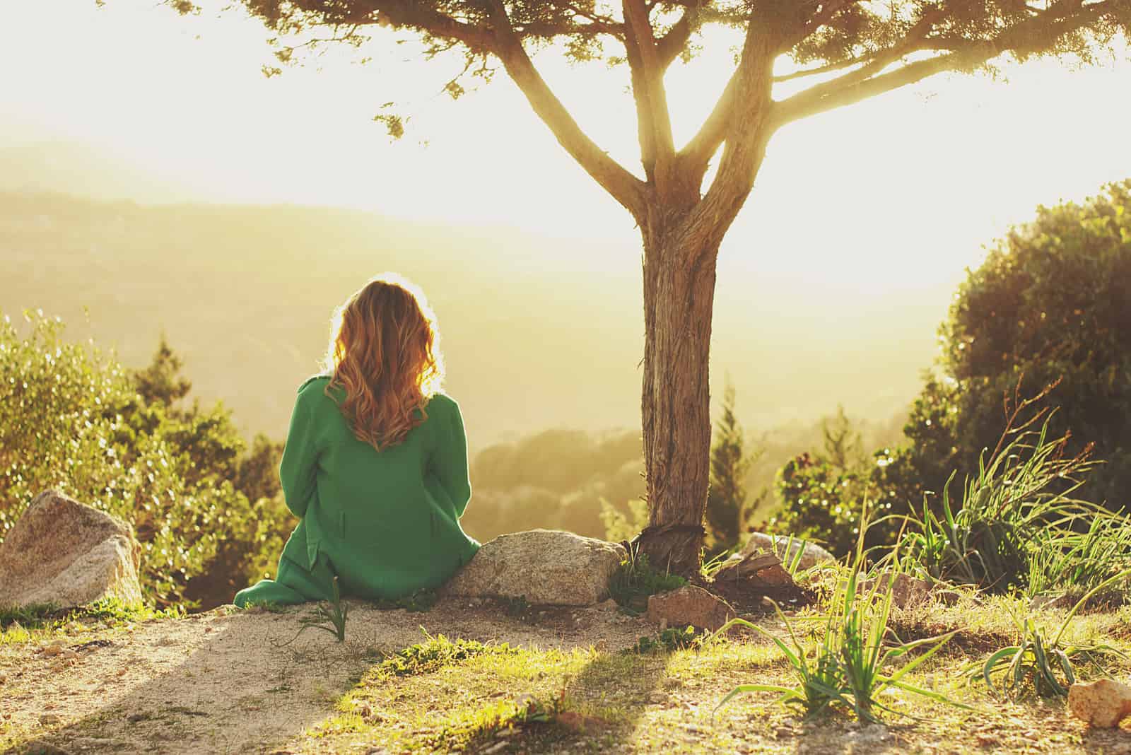 una donna dai lunghi capelli biondi siede su una roccia e guarda in lontananza