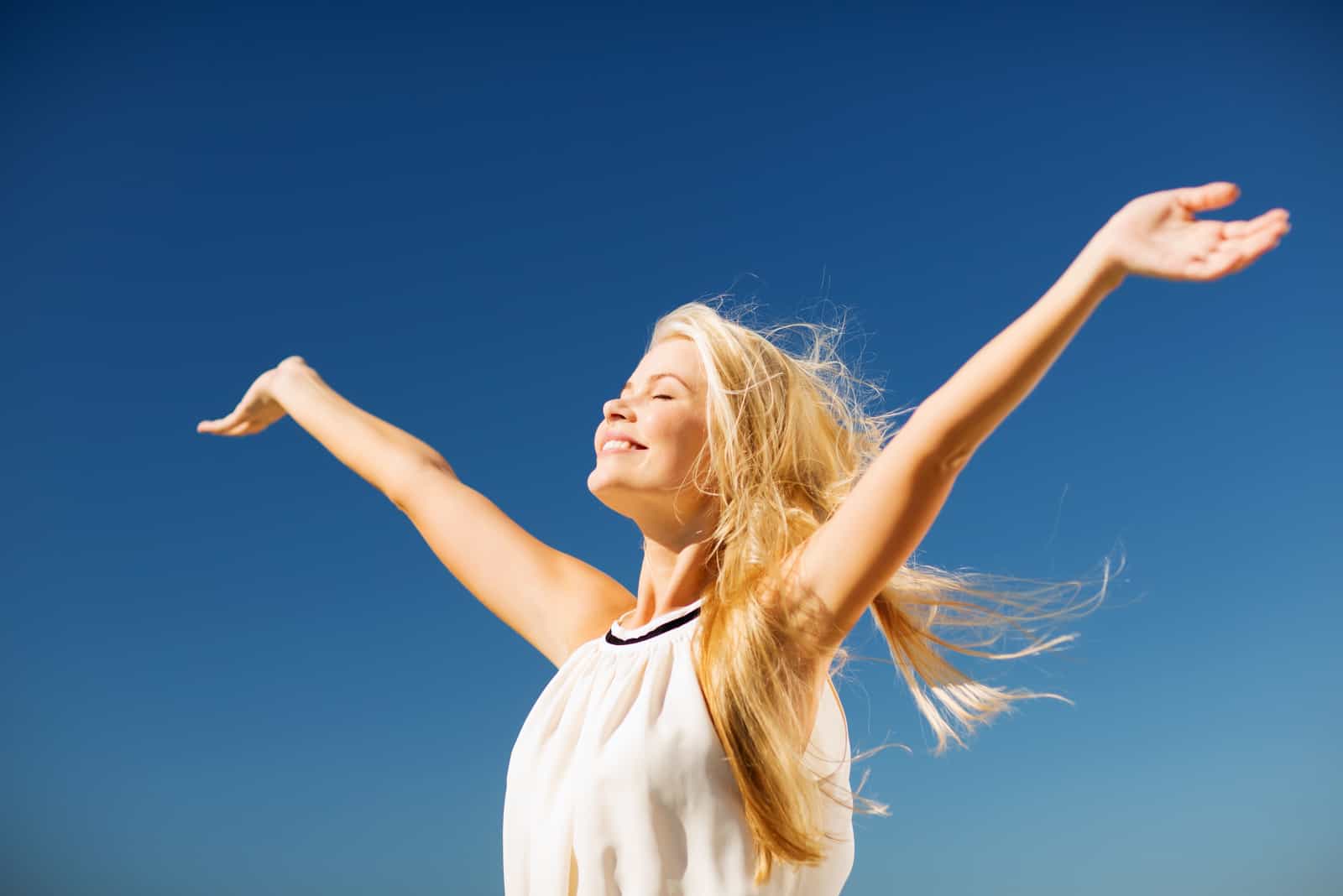 a woman with long blonde hair stands with her arms outstretched