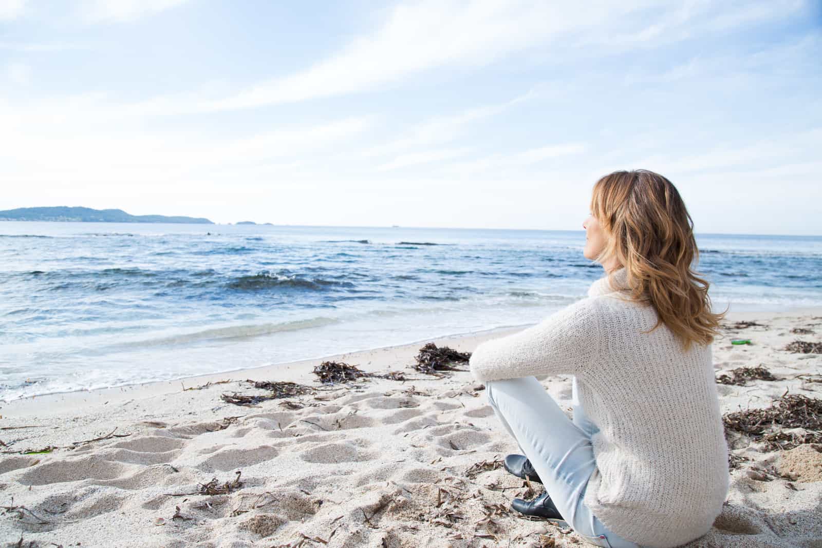 una mujer de pelo largo y castaño está sentada en la playa