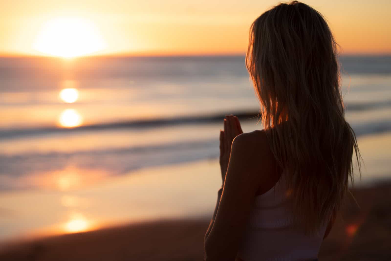 una donna con lunghi capelli castani è in piedi sulla spiaggia e guarda il mare