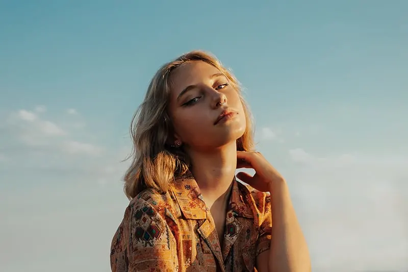 blonde woman touching neck with hand under blue sky