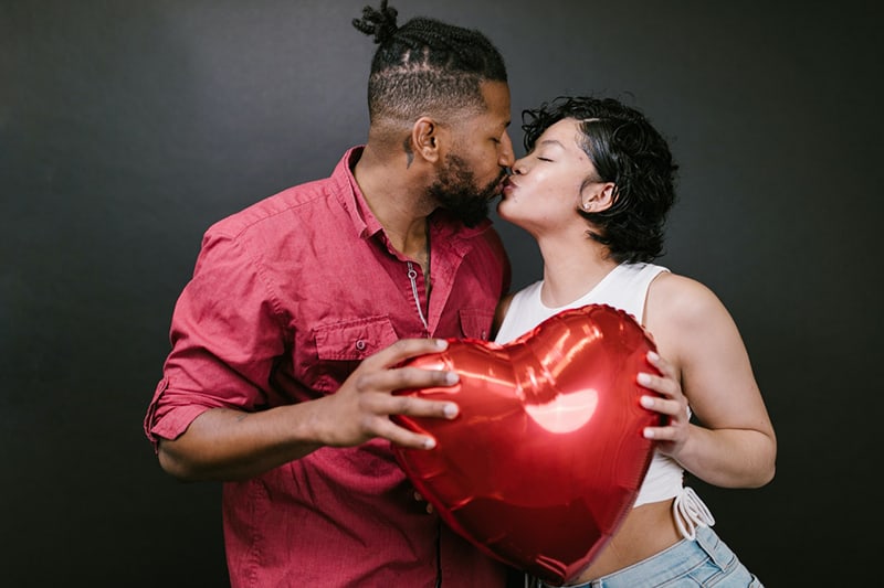 loving couple kissing while together holding a heart-shaped balloon